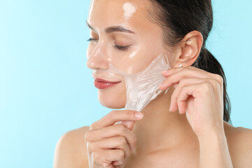 Poster - Beautiful woman peeling off face mask on light blue background, closeup