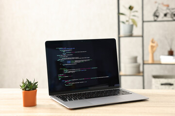 Programmer's workplace. Modern laptop with unfinished code and houseplant on desk indoors