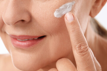 Poster - Senior woman applying face cream on white background, closeup