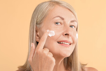 Canvas Print - Senior woman applying face cream on beige background