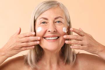 Poster - Senior woman with face cream on beige background