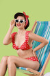 © New Africa - Pin-up woman in bikini on folding chair against green background