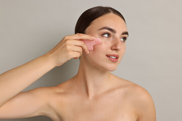 Canvas Print - Beautiful young woman doing facial massage with gua sha tool on grey background