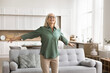 © fizkes - Attractive older 65s retired woman standing with her arms outstretched and joyful expression, feeling excitement, enjoy moment of freedom, welcoming new happy day, spend pastime in modern living room