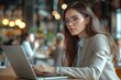 © Pooja - Side view of brunette business woman in glasses wearing beige suit working on laptop while sitting at table in company office with colleagues in, Generative AI