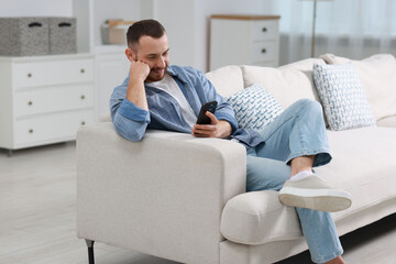 Poster - Handsome man using smartphone on sofa indoors