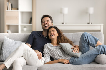 Joyful married couple in love resting on comfortable sofa, hugging with affection, trust, talking, laughing, having fun together, enjoying romantic leisure, boning, romance at home