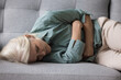 © fizkes - Aged woman clutching her stomach lying on sofa suffers from strong abdominal pain, chronic disease, discomfort, looks unhealthy, lack of energy or motivation, symptom of depression or physical ailment