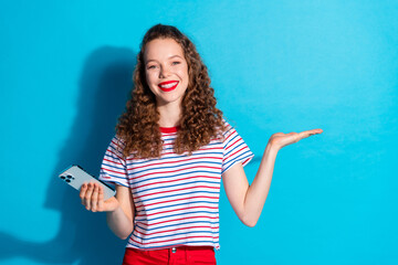 Wall Mural - Happy woman with curly hair holding phone smiling confidently against blue background