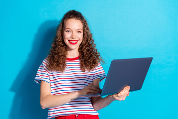 Wall Mural - Cheerful young woman in striped shirt using laptop against vibrant blue background