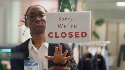 Wall Mural - African american smiling storekeeper closing clothing store at night after selling entire inventory. BIPOC retail worker turning opened message sign on fashion boutique door in mall department