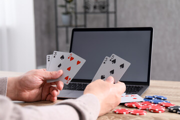 Sticker - Online poker. Man with playing cards, chips and laptop at wooden table indoors, closeup