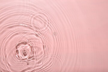 Rippled surface of clear water on pink background, top view