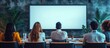 © MBRAMO - Back view of a group of people sitting around a table, facing a blank white screen.