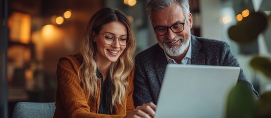 Canvas Print - A young woman and an older man smiling while looking at a laptop in a cafe.