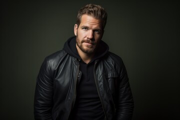 Handsome young man in a black leather jacket on a dark background.