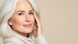 © M - Elegant mature woman with silver hair, touching her face gently, radiating confidence against a soft neutral background