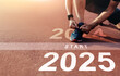 © Urupong - New year 2025 concept, beginning of success. Text 2025 written on asphalt road and male runner preparing for the new year. Concept of challenge or career path and change.