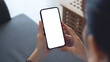 © tippapatt - Cell phone white blank screen mockup, woman's hand holding mobile phone with blank screen and a cup of coffee in coffee shop, over shoulder view