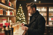 © t.sableaux - A man examines perfume bottles in a warm, inviting boutique with holiday decorations and a Christmas tree