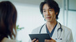 © ABX - Smiling Japanese doctor holding tablet in patient consultation