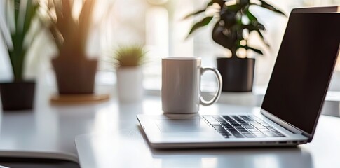 Wall Mural - Minimalist white office desk with laptop and coffee mug on a blurred background, with space for text, representing the concept of working from home