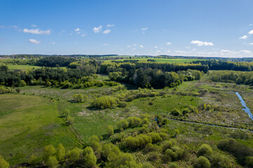 A bird's eye view of green forest and field. Wetlands nearby. Clear blue sky, sunny day. 