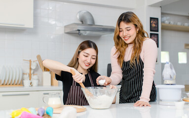 Cute happy two young Asian female friends, woman wearing aprons, preparing dessert tasty sweet for party cooking dough baking cakes. Concept hobby enjoy weekends in kitchen teenage lifestyle at home.