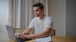 © stockbusters - Serious man working remotely on laptop at home desk. Smart businessman typing