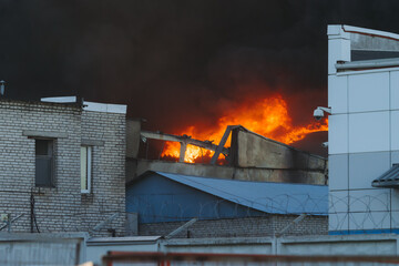 Wall Mural - Massive large blaze fire in the city, blazing warehouse factory, storage building is burning, firefighters team putting out the fire, firemen on duty, extinguish the fire, arson, burning house damage