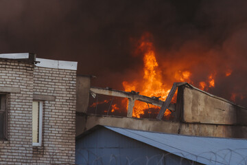 Wall Mural - Massive large blaze fire in the city, blazing warehouse factory, storage building is burning, firefighters team putting out the fire, firemen on duty, extinguish the fire, arson, burning house damage