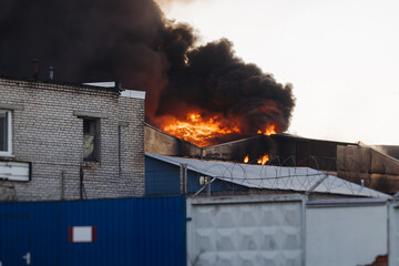 Wall Mural - Massive large blaze fire in the city, blazing warehouse factory, storage building is burning, firefighters team putting out the fire, firemen on duty, extinguish the fire, arson, burning house damage