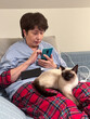 © satura_ - Elderly woman using smartphone and social networks with a siamese cat on their lap, relaxing on a couch in cozy indoor