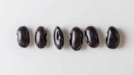 A row of black beans are lined up on a white background