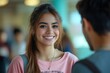 © Yash - Portrait of smiling Hispanic female student in pink oversized shirt leaning on hand and talking amiably to male classmate during break at university, Generative AI