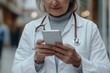 © Ananya - Aged female general practitioner holding modern smart phone in hands, close up screen view with white mock up, doctor working on-line, making calls, check schedule, jotting information, takes
