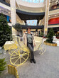 © satura_ - Woman in casual attire standing next to a decorative carriage in a modern shopping mall. Christmas holiday decorations and festive atmosphere create a lively and cheerful scene