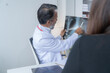 © Tj - Senior male doctor is pointing at an x-ray image while explaining something to a female patient during a medical consultation