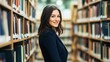 © Mohammed - Smiling woman in a dark blue blazer stands in a library, surrounded by bookshelves.