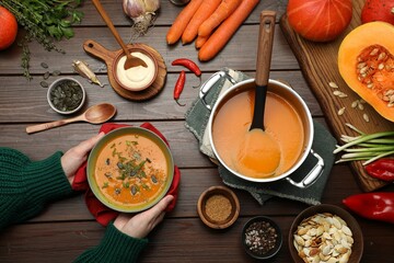 Poster - Woman with delicious pumpkin soup at wooden table, top view