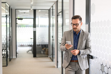 Wall Mural - serious young man in eyeglasses messaging online over mobile phone while standing in office corridor