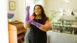 © AntonioDiaz - Cheerful woman dons black apron and purple rubber gloves, prepared to tackle household tasks