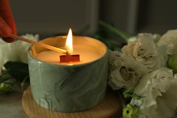 Wall Mural - Woman lighting candle at table with beautiful flowers, closeup