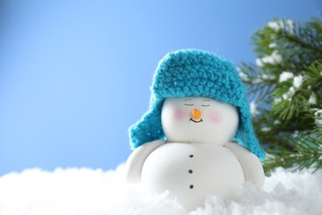 Canvas Print - Cute decorative snowman on artificial snow against light blue background. Space for text