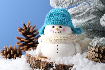 Sticker - Cute decorative snowman, fir tree branches and cones on artificial snow against light blue background, closeup