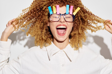 Wall Mural - Happy woman with curly hair and colorful clips posing playfully against a bright white background, showcasing her joyful expression and trendy style