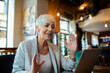 © Davor - Senior businesswoman having video call on laptop in cafe