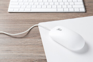 Computer mouse with mousepad and keyboard on wooden desk, closeup