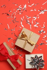 Poster - Shiny confetti and gift boxes on red background, flat lay