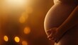 © narak0rn - Pregnant woman gently holding her baby bump, warm and soft glow in the background.
